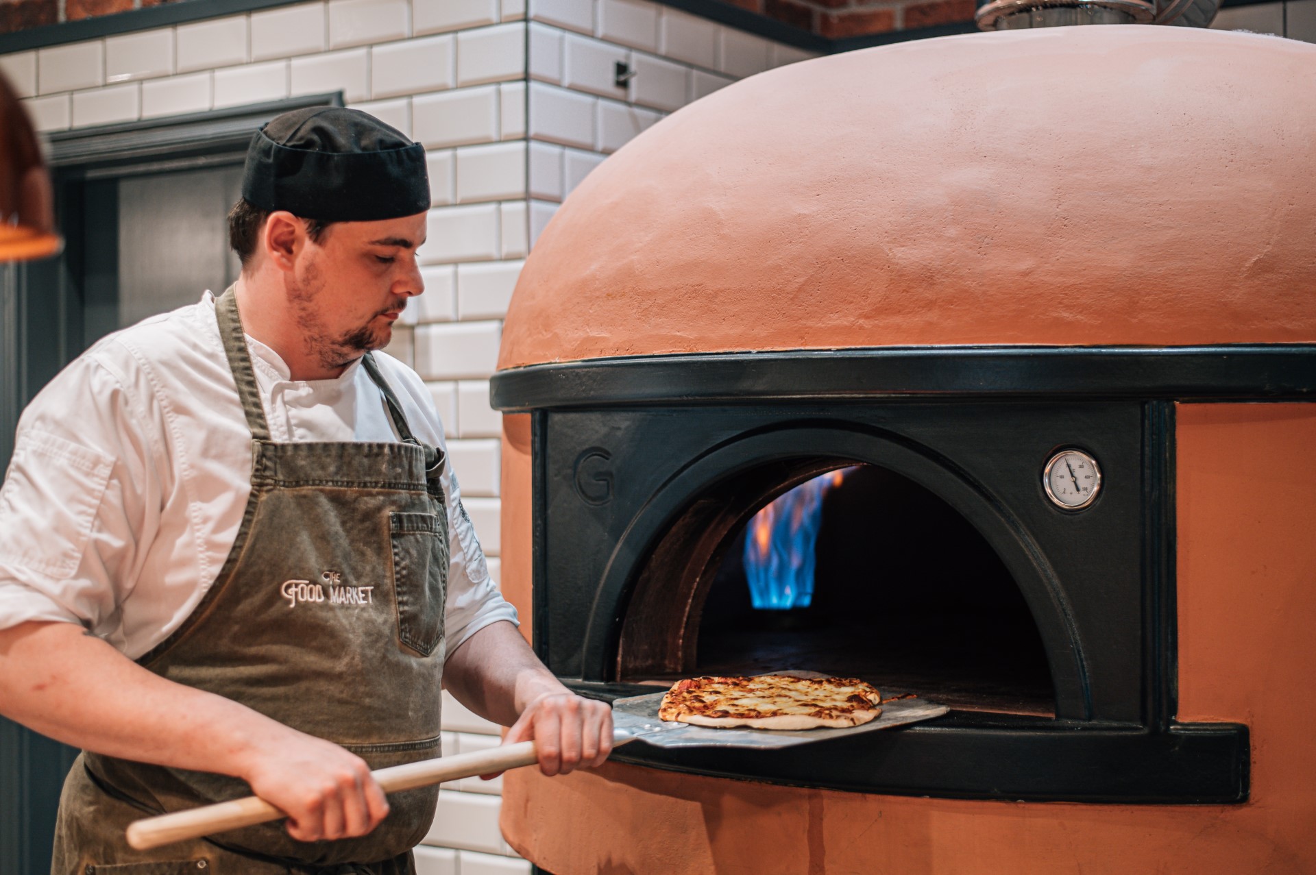 chef taking pizza out of brick oven with peel