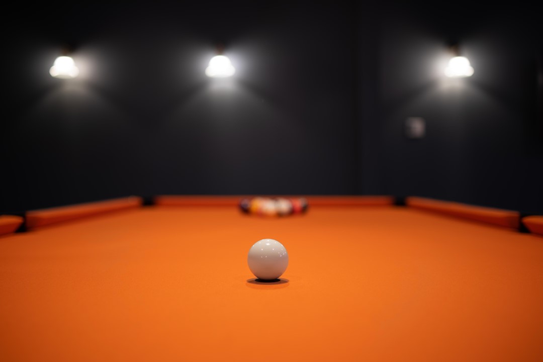 white cue ball on orange pool table with lights above