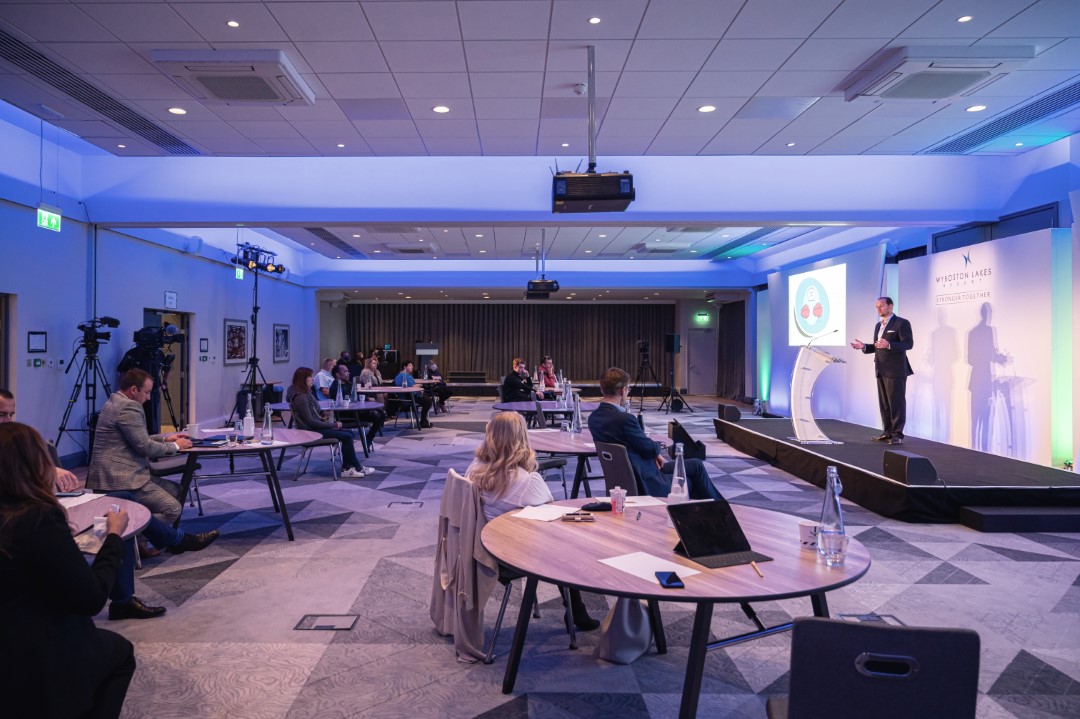 conference room with spaced seating and speaker on stage