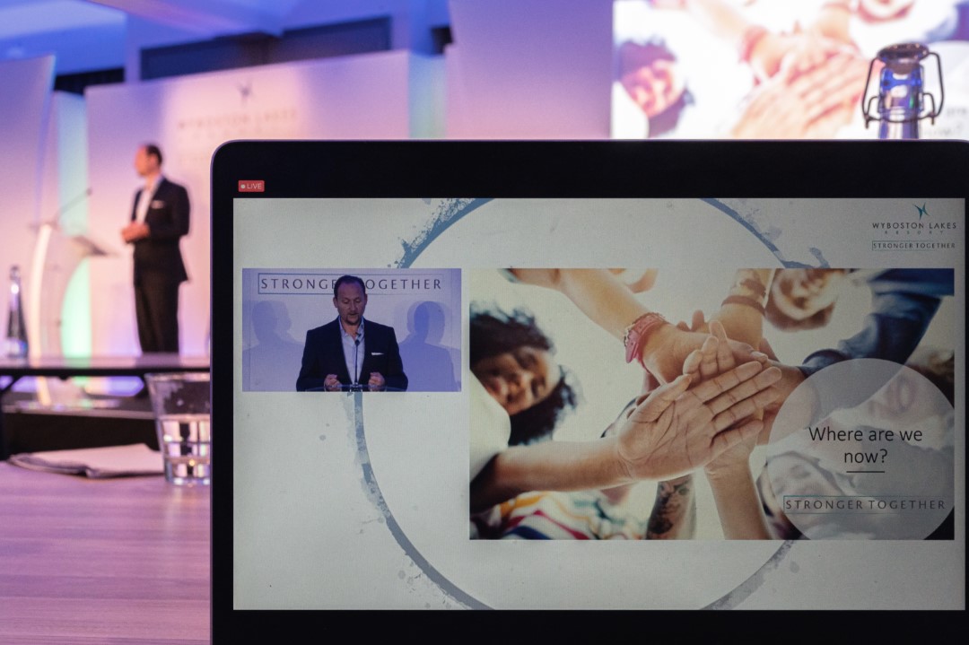 man speaking at conference presentation screen with group hands together