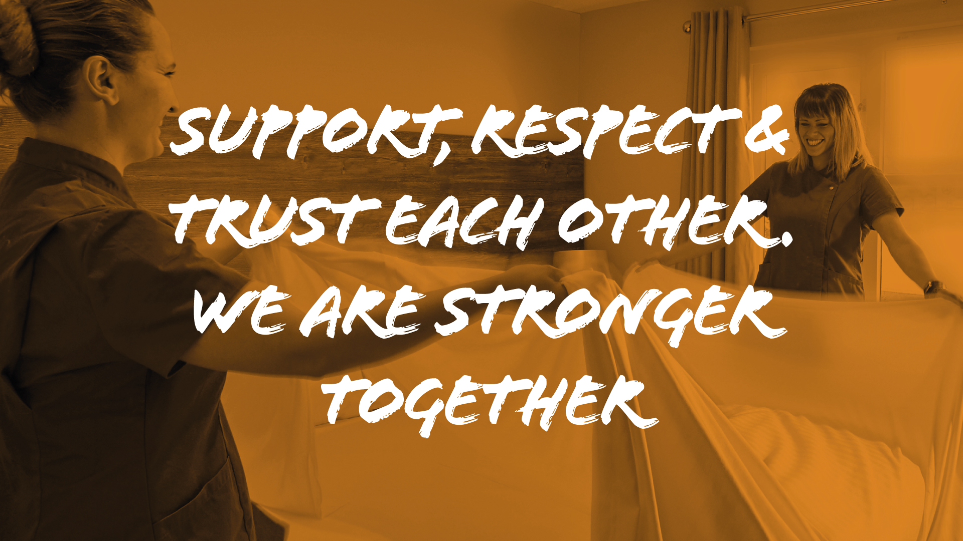 two women smiling making bed together in room