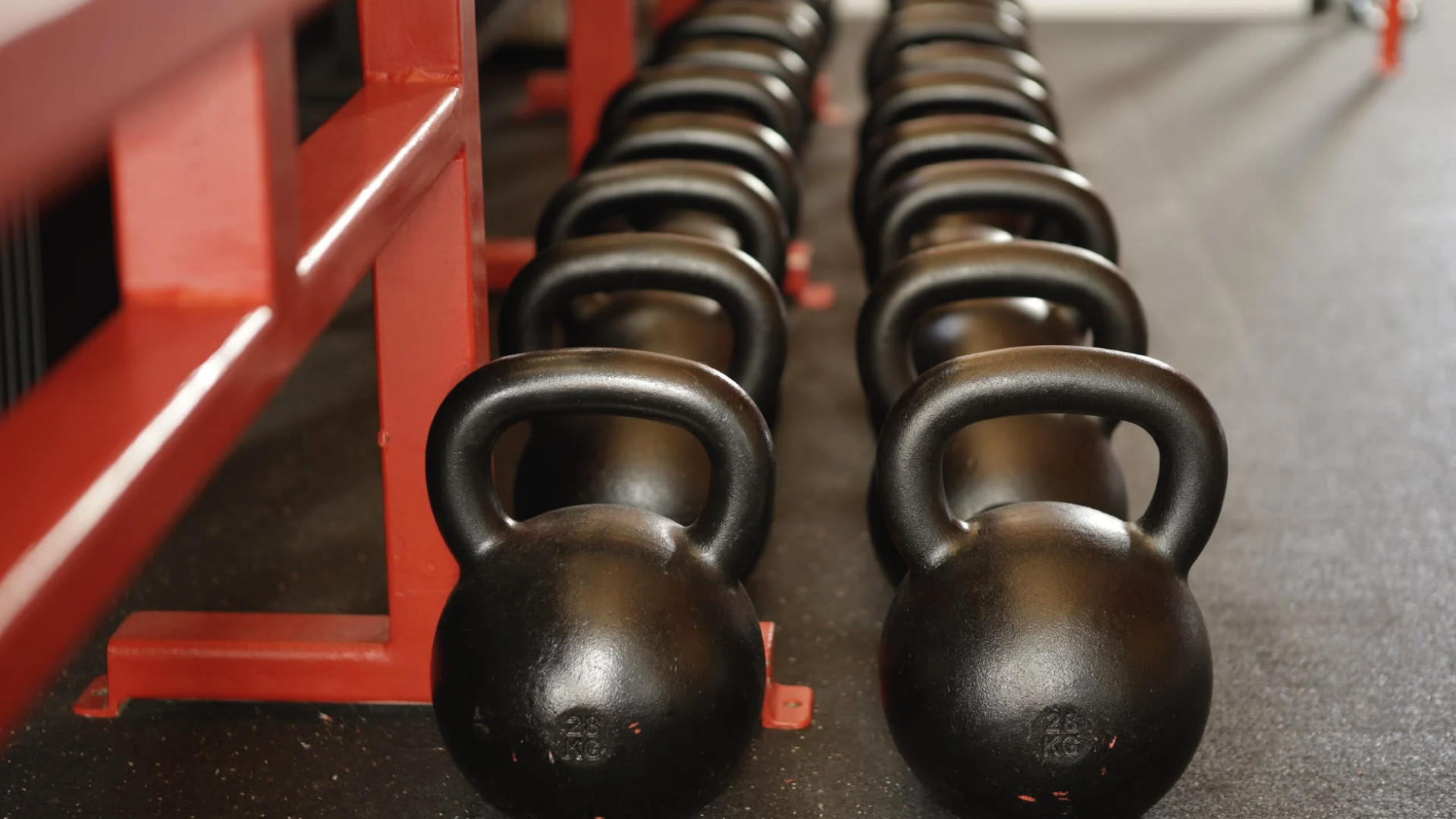 rows of black kettlebells next to red metal rack