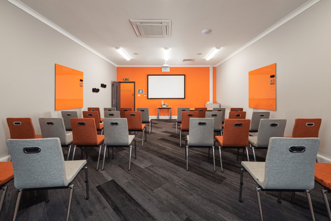 room with orange and grey chairs facing whiteboard and projector
