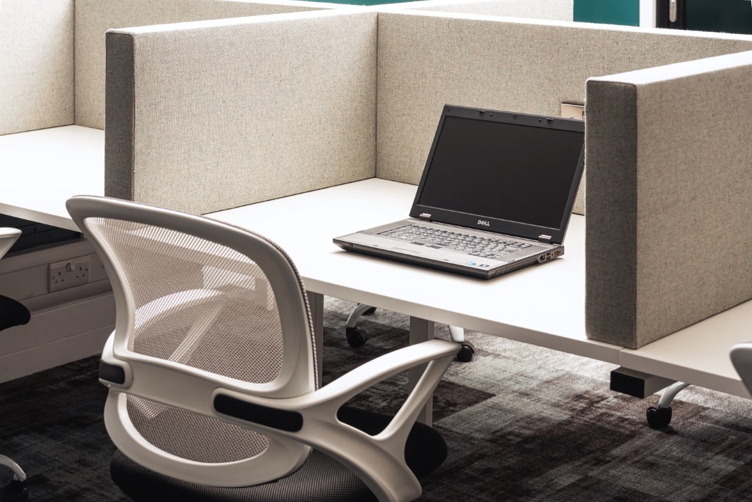 empty office desk with laptop and mesh chair