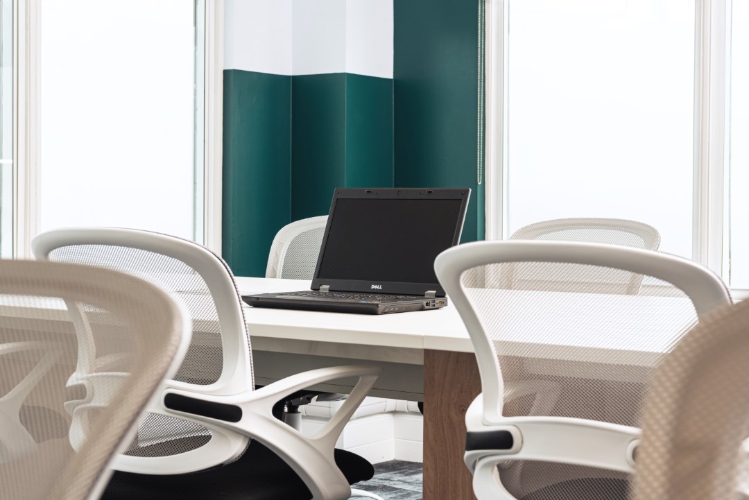 laptop on white table surrounded by white mesh office chairs
