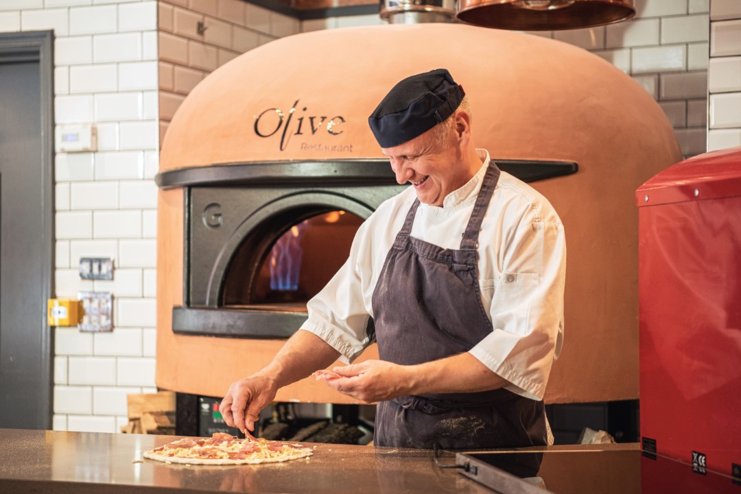 chef preparing pizza in front of a pizza oven