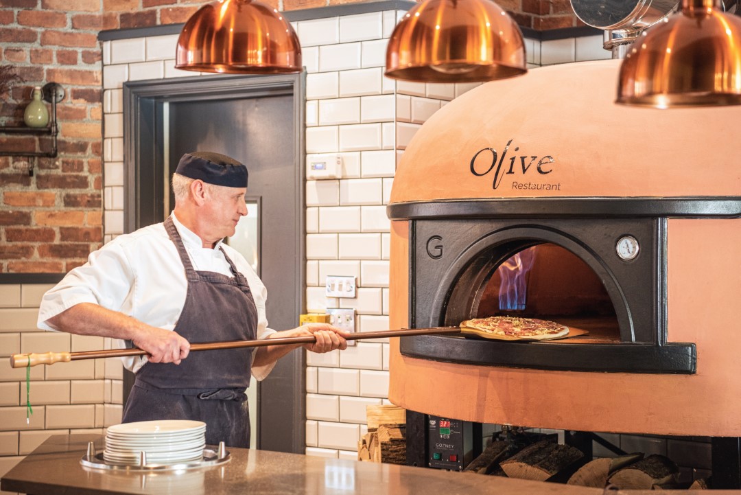 chef placing pizza in large wood fired oven
