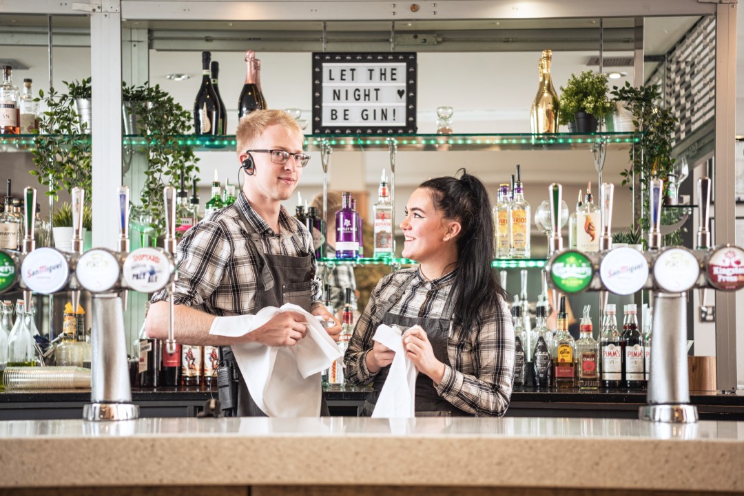 two bartenders cleaning glasses behind bar counter (1)