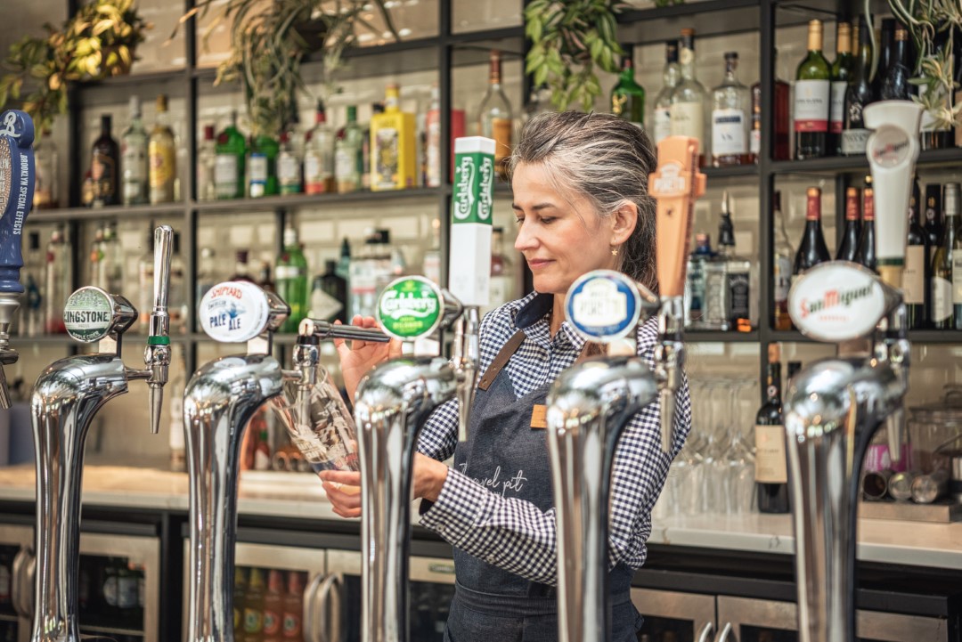 woman pouring beer behind bar with taps and bottles