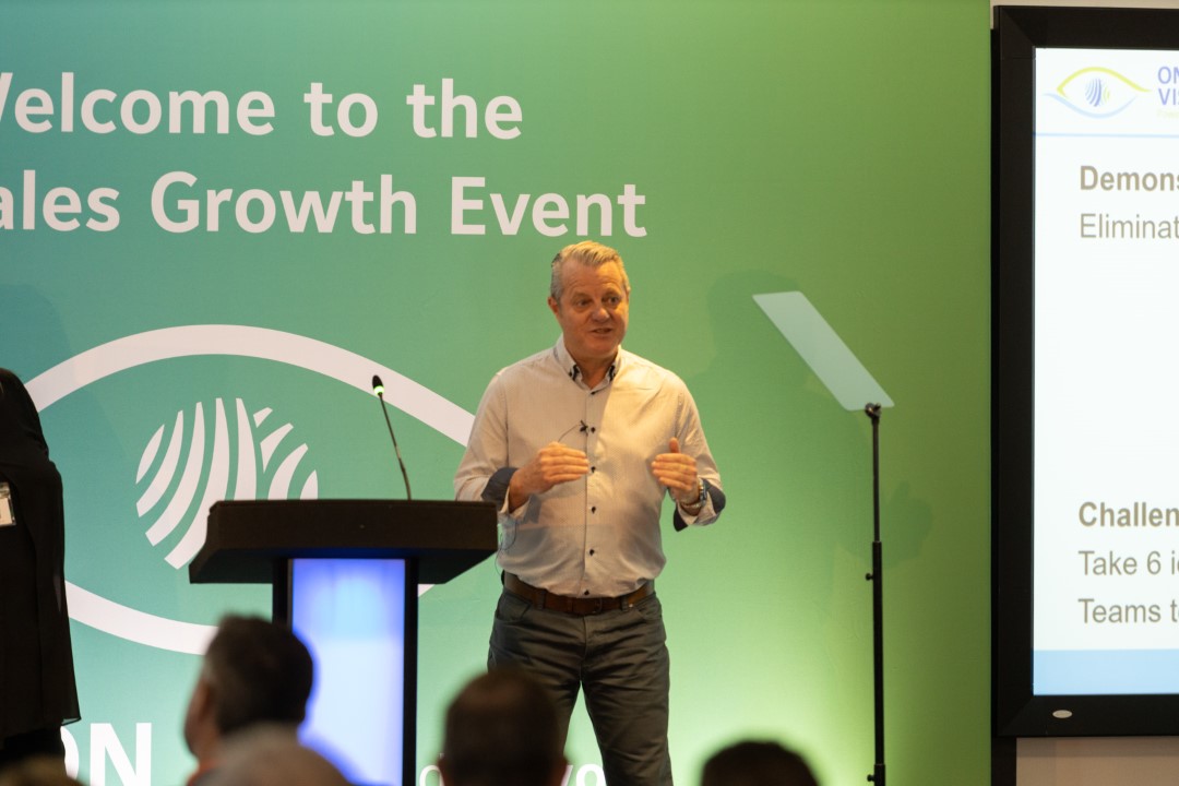 man speaking at podium with green backdrop