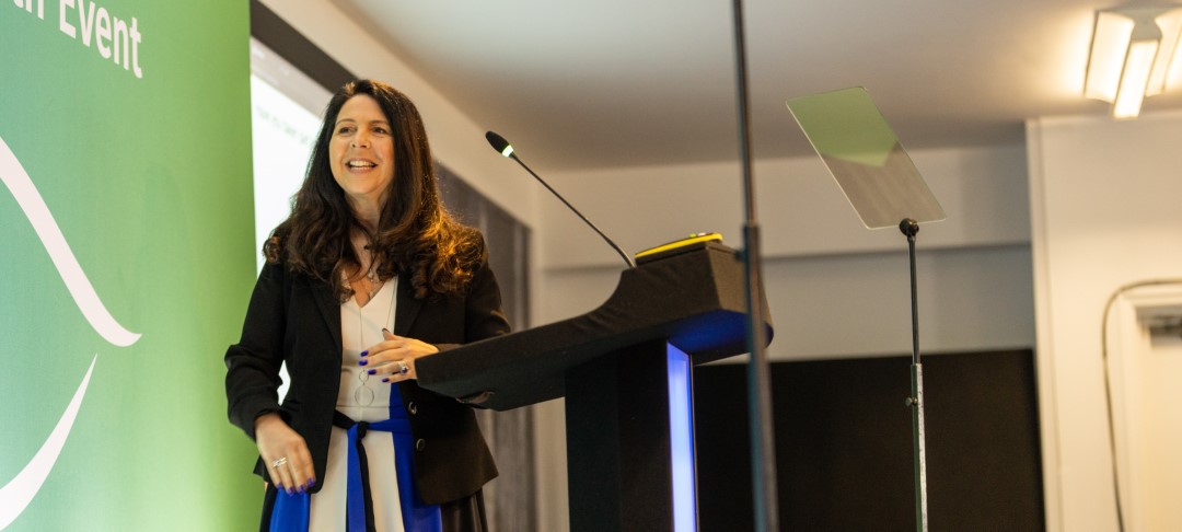 woman speaking at lectern with microphone and teleprompter in room