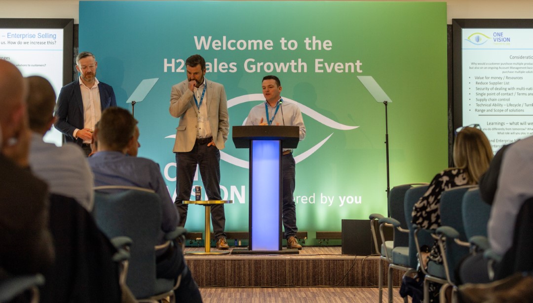 three men speaking on stage at business event