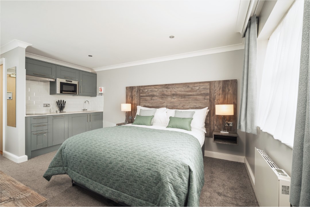 double bed with green bedding next to small kitchen area