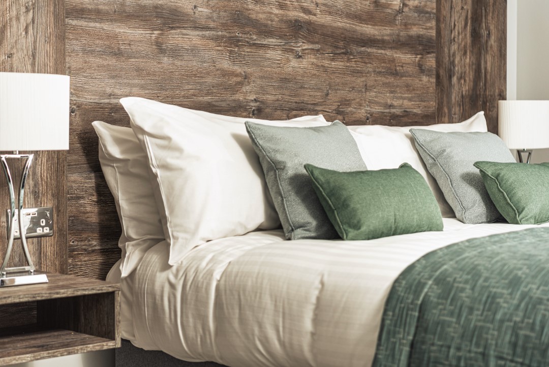 bed with white sheets and green cushions on wooden headboard