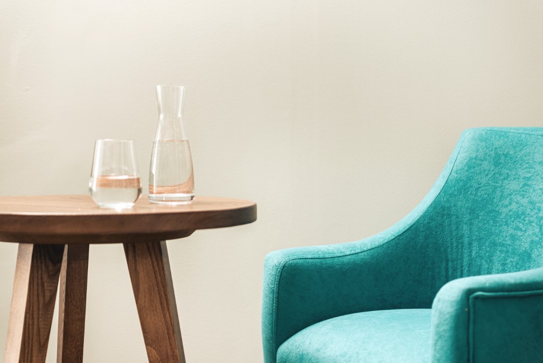 turquoise armchair beside wooden table with water carafe and glass