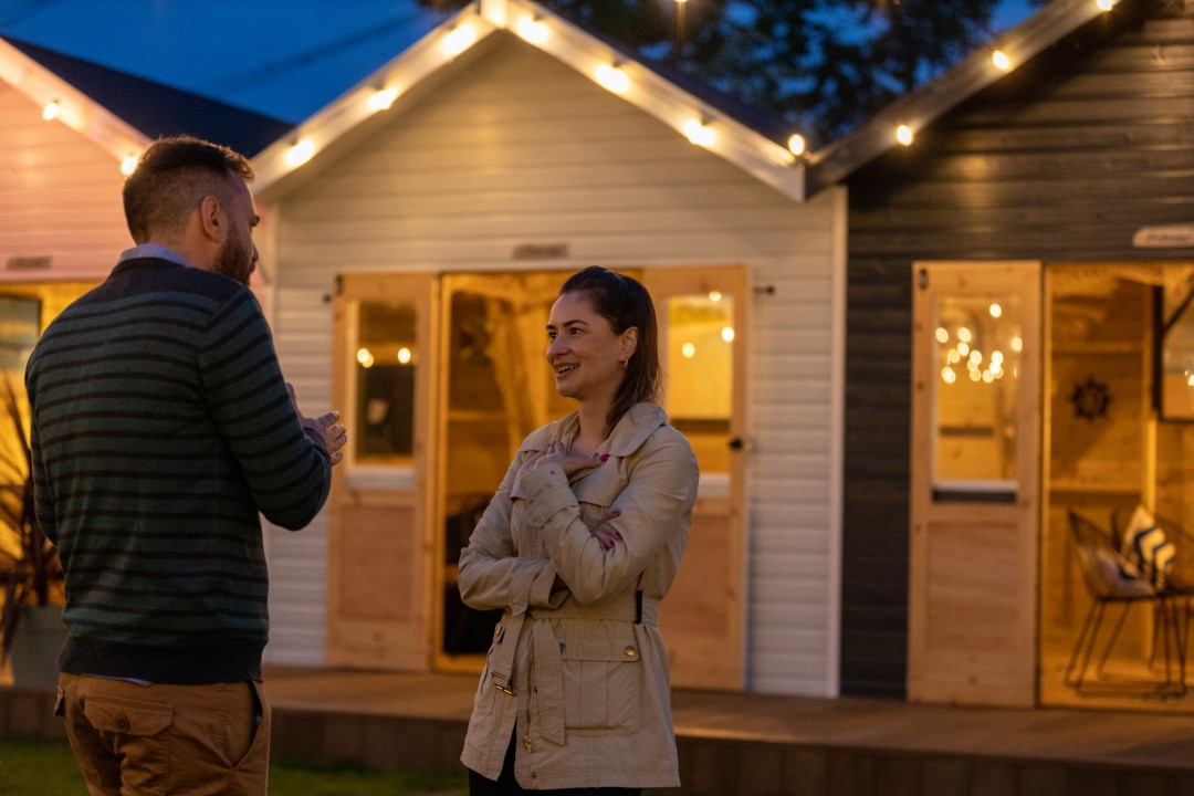 man and woman talking outside wooden cabins at dusk