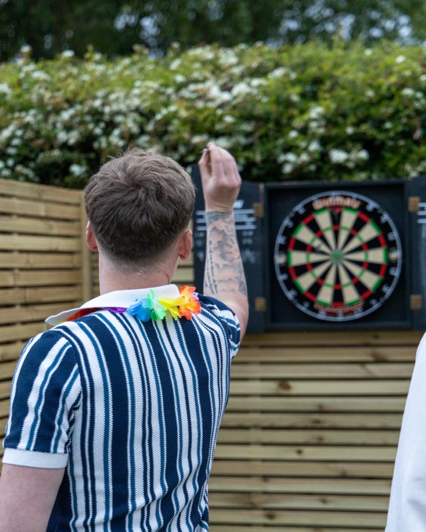 man with tattoo throwing dart at dartboard outside