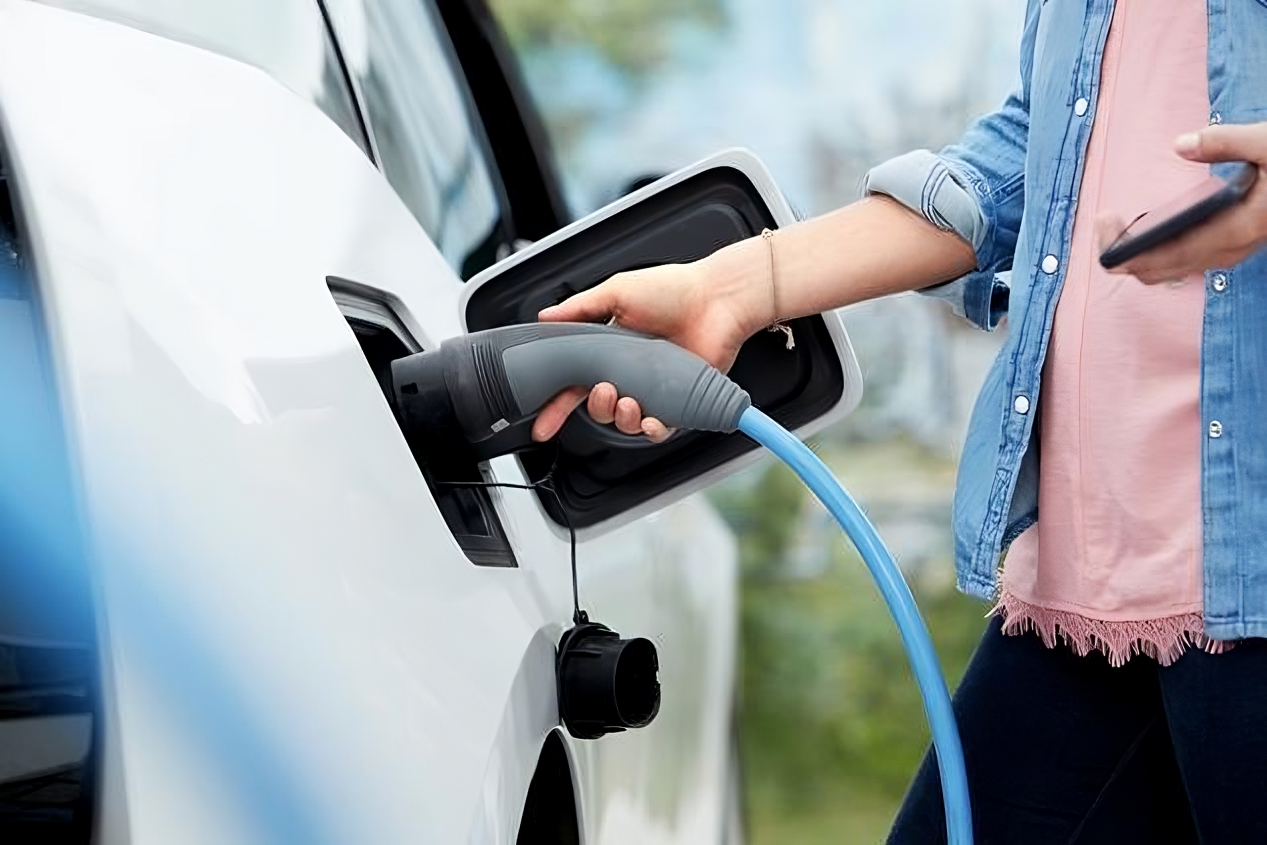 person plugging in electric car charger with phone in hand