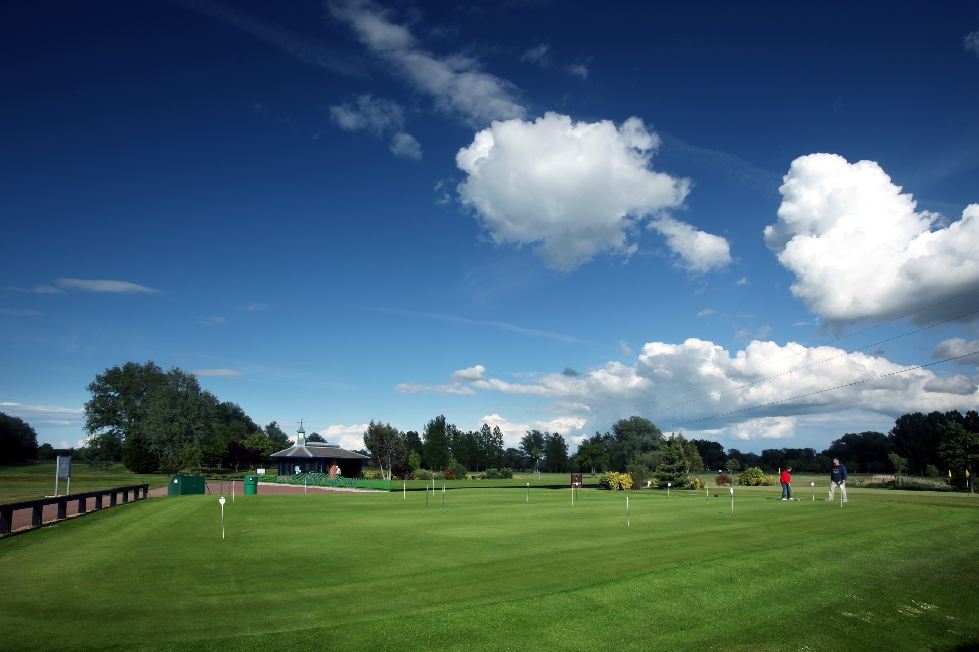 golf course green with two people playing under blue sky