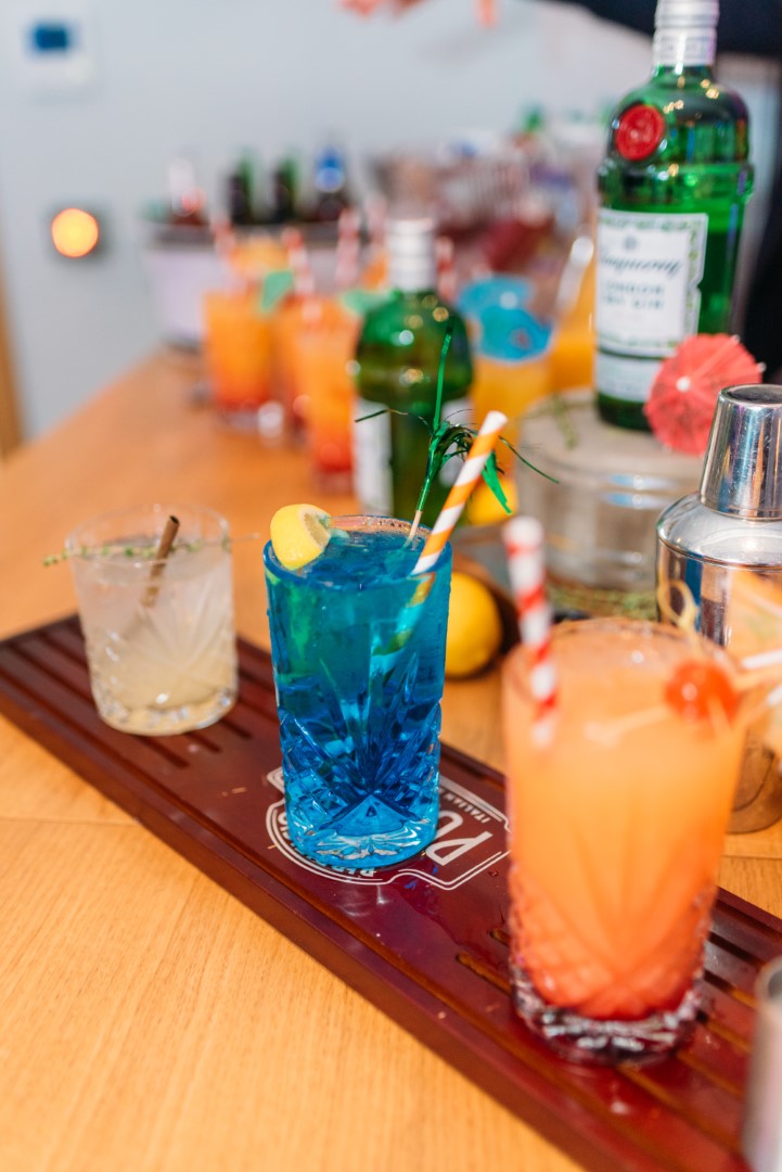 three colourful cocktails on a wooden bar surface