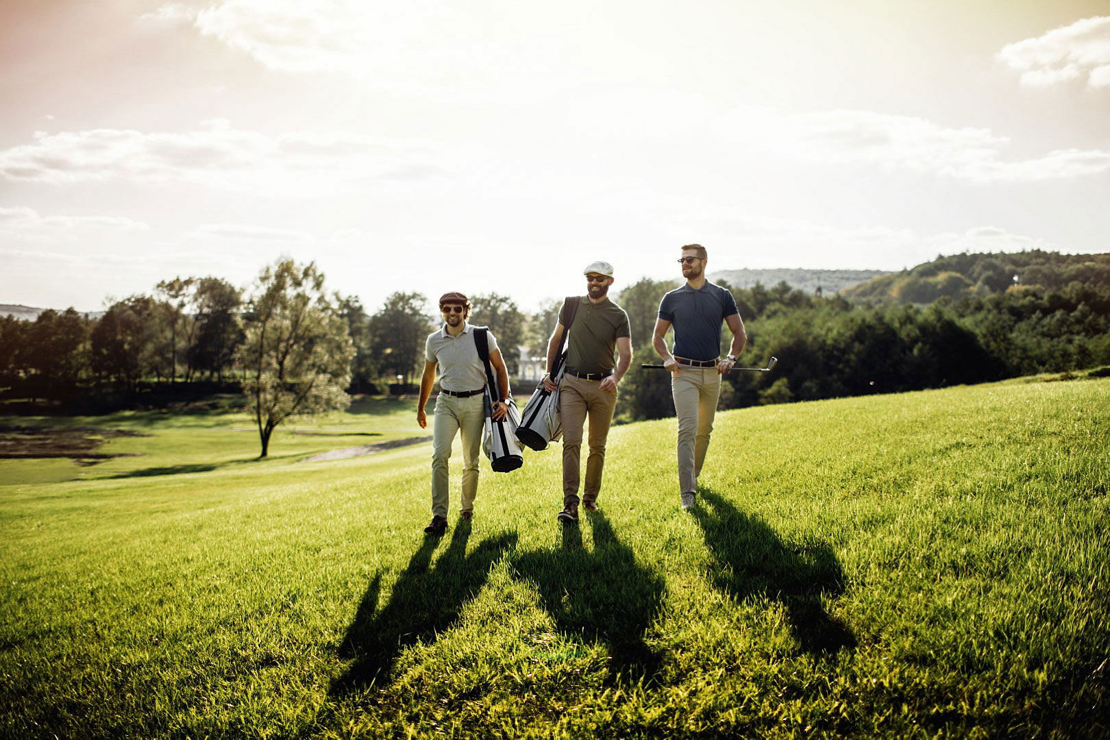 three men walking on grassy hill with golf bags and