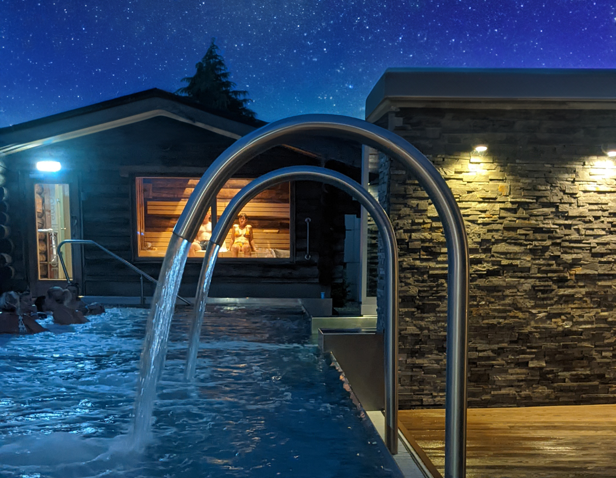 nighttime outdoor pool with people and wooden sauna
