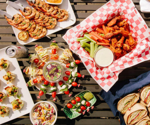 platter of prawns chicken wings vegetables and sandwiches on table