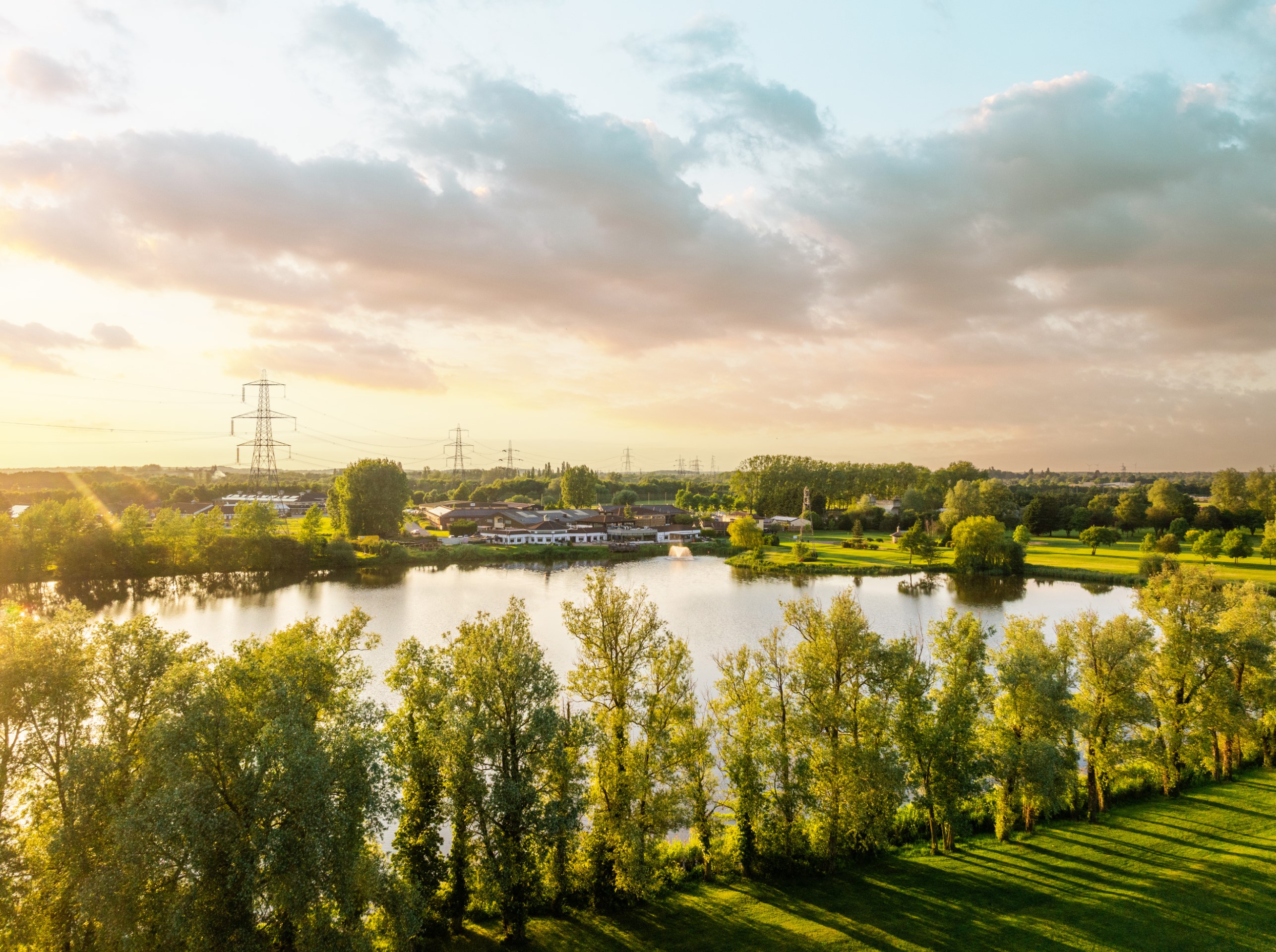 lake with surrounding trees green fields and buildings at sunset