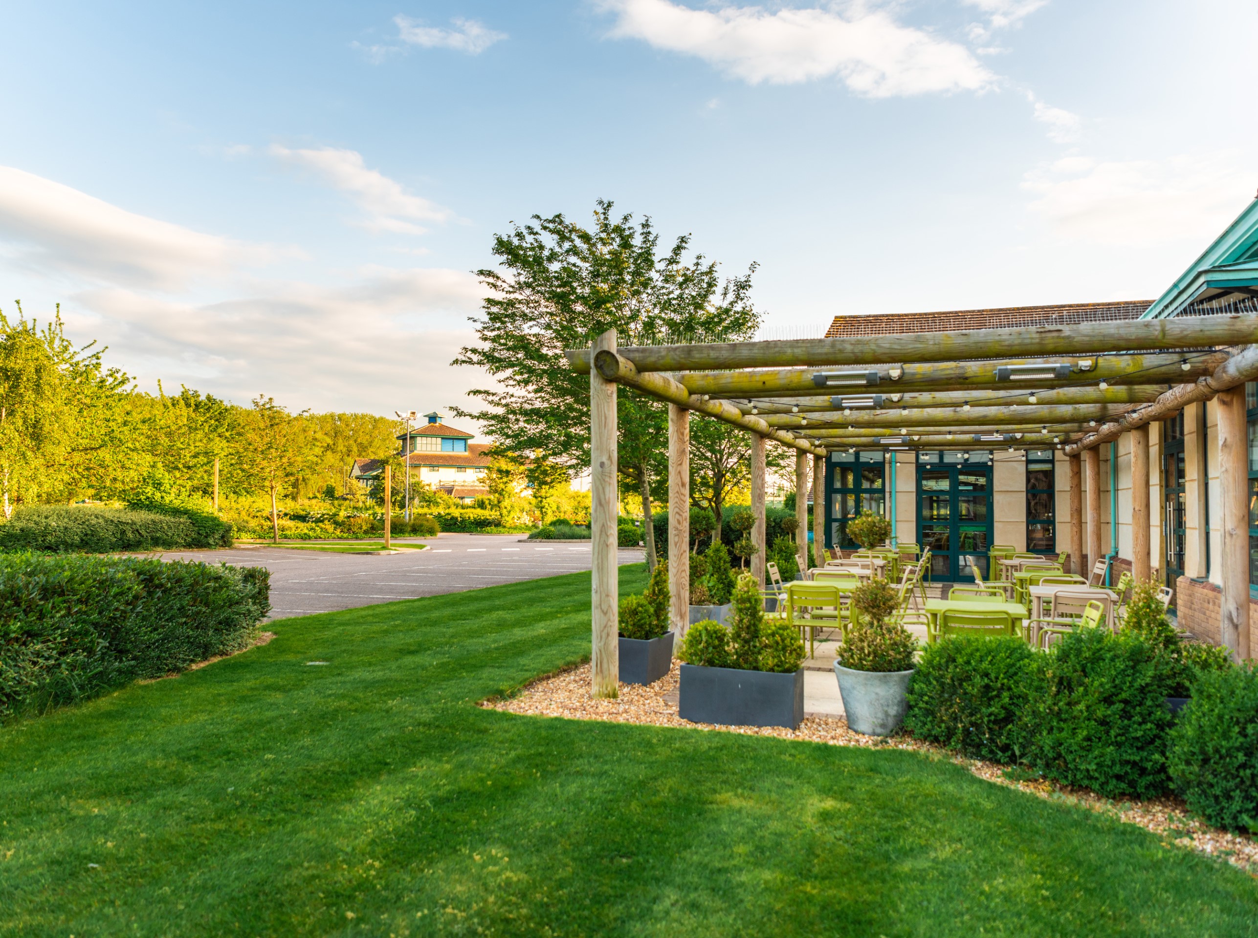 empty outdoor seating area with wooden pergola and green chairs