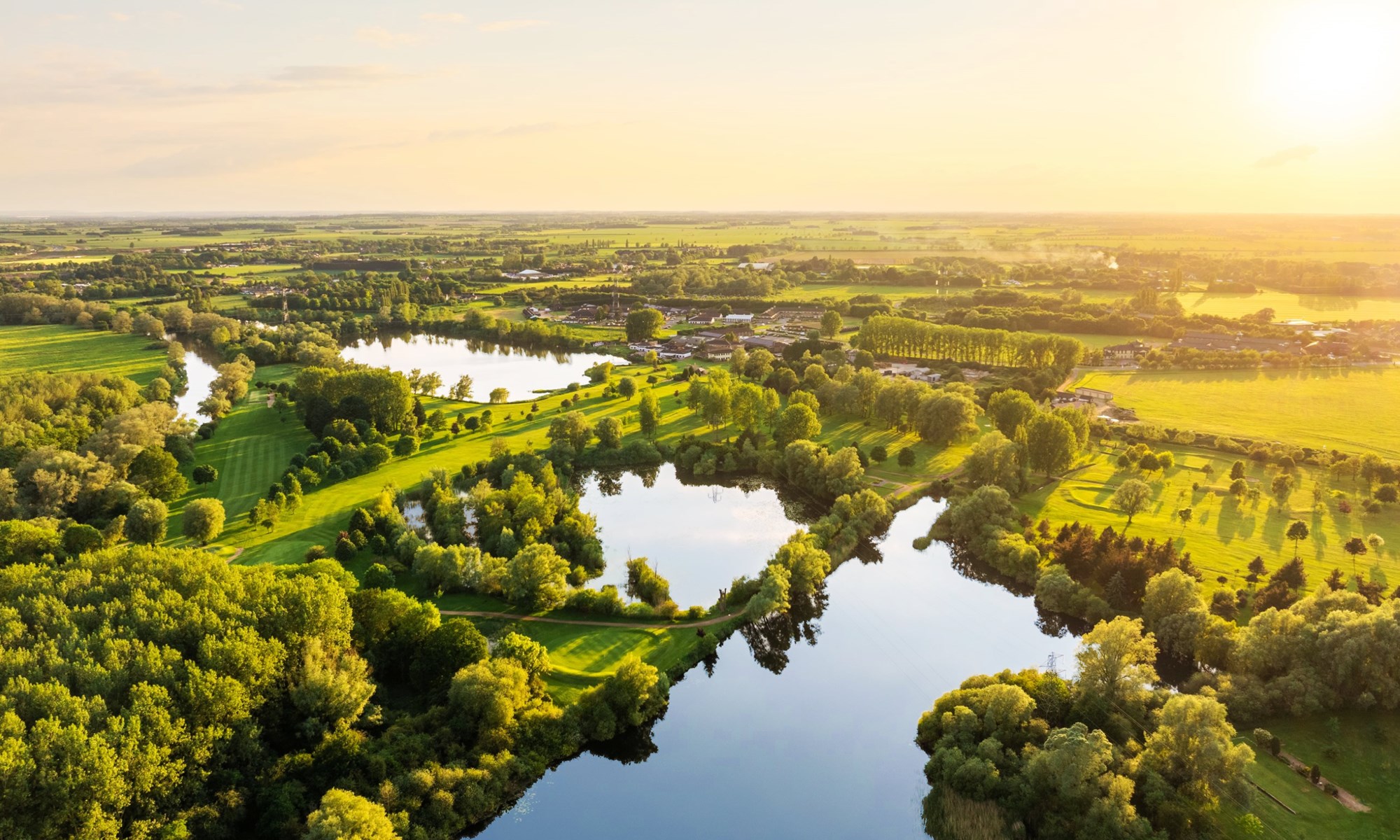 river flowing through green trees and fields at sunset