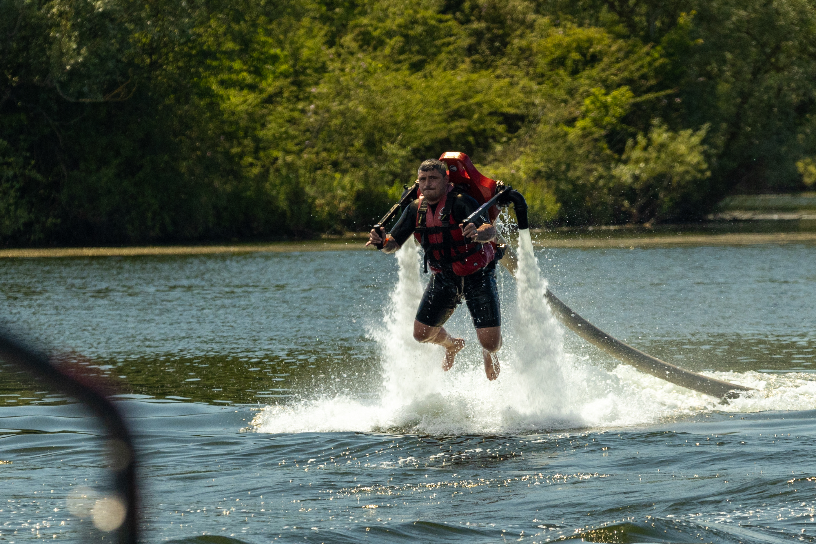 man flying over lake using water jetpack with green trees