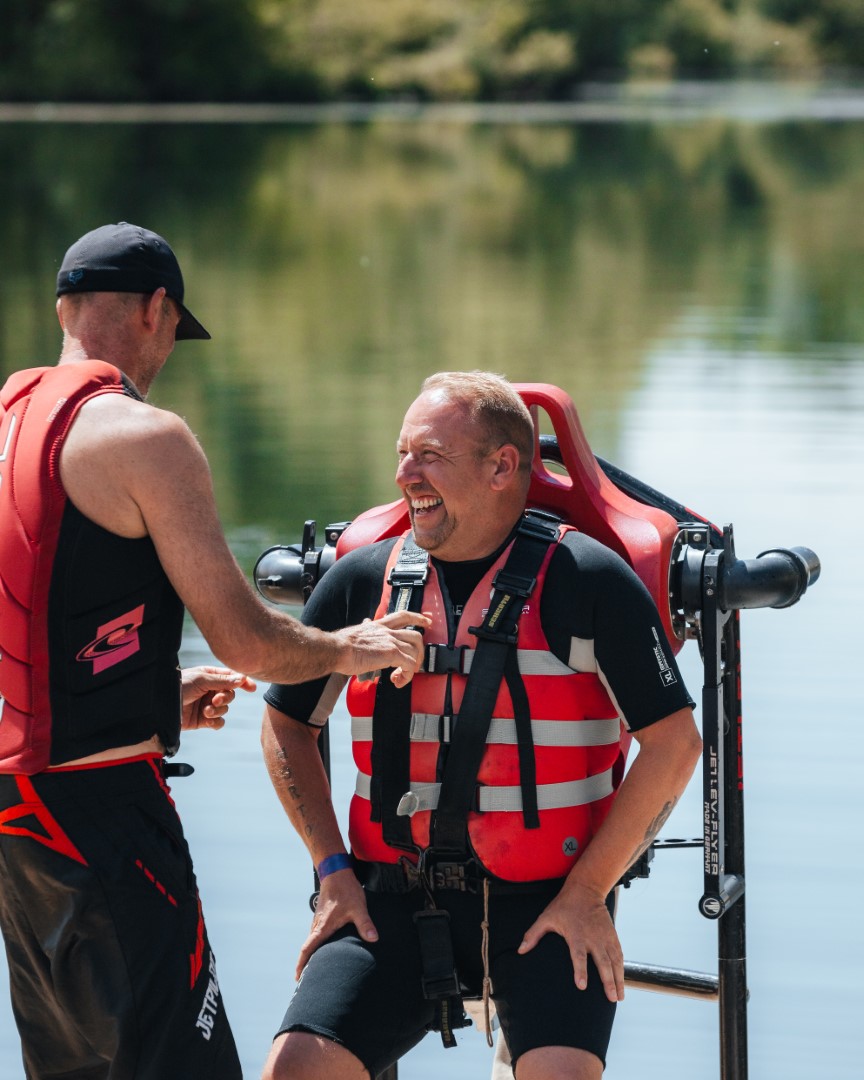 two men with life jackets by lake one wearing jetpack