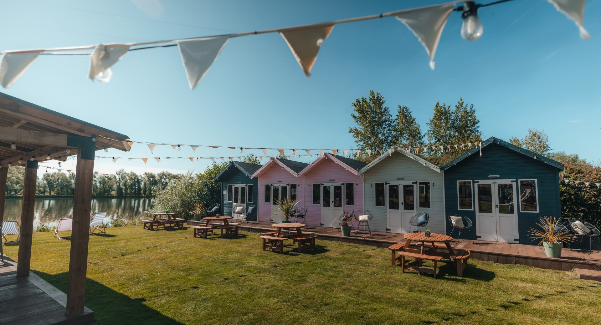 colourful beach huts lawn picnic benches lake sky bunting chairs
