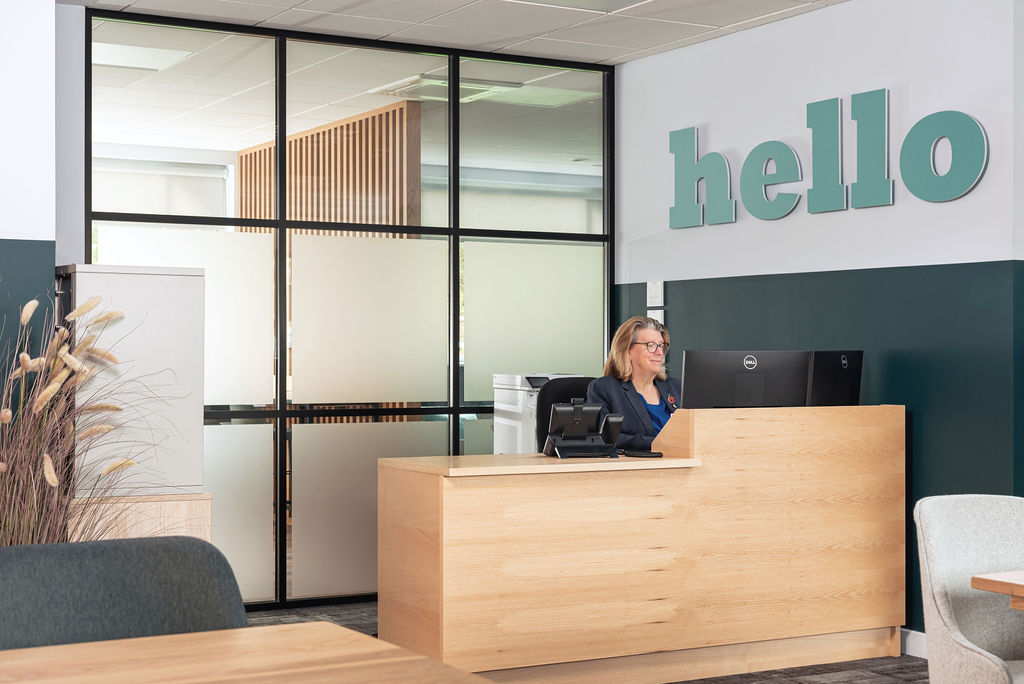 woman sitting at wooden reception desk with hello sign