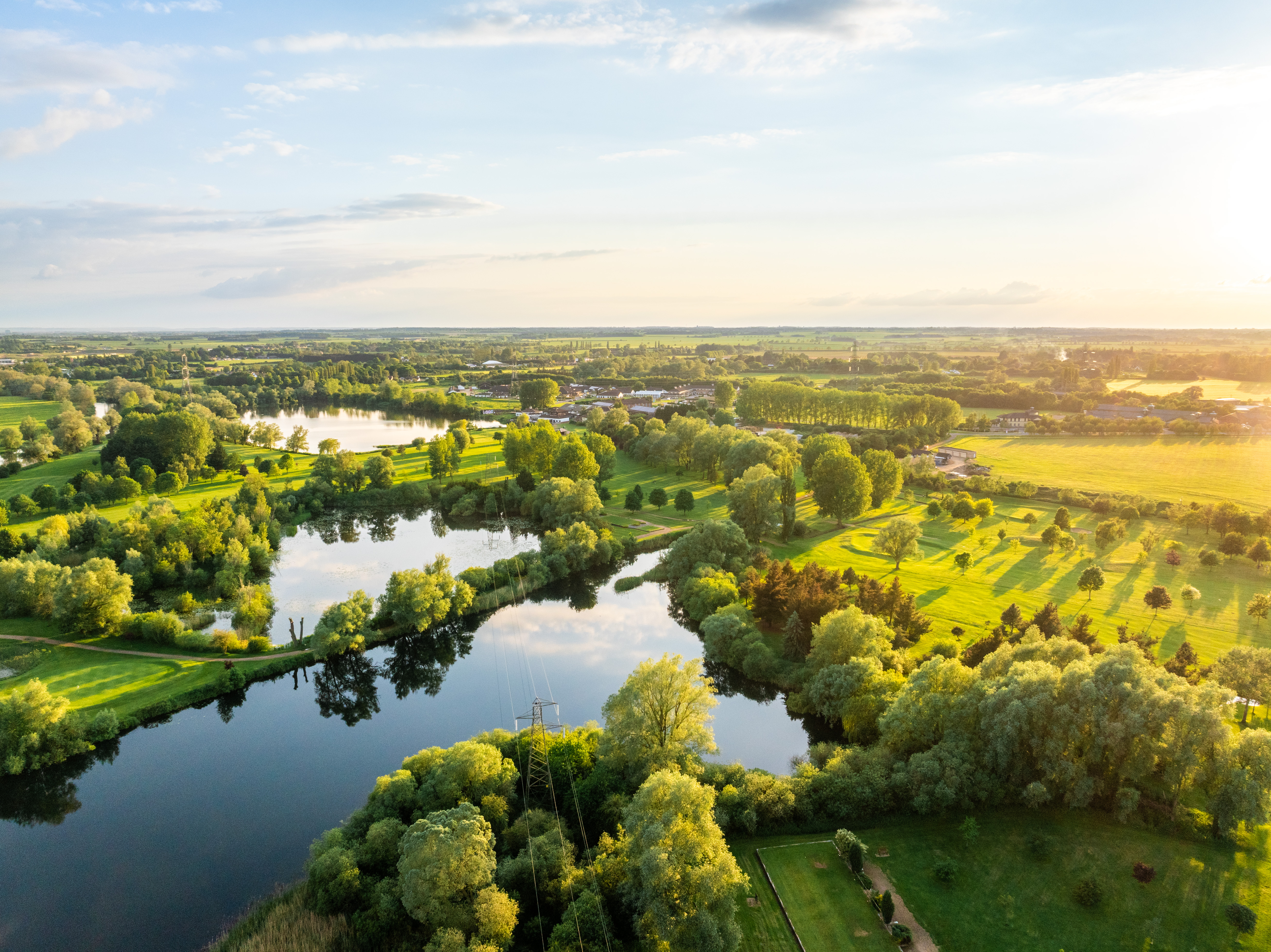 aerial view of river and green fields in sunlight