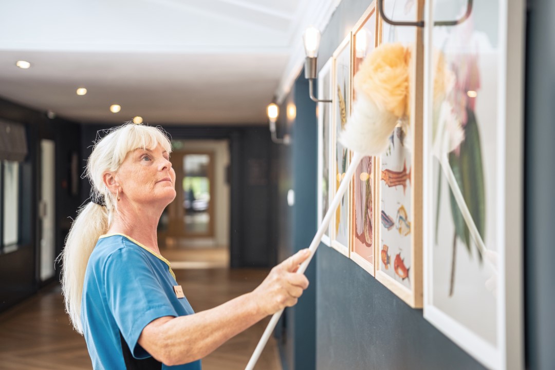 woman dusting framed pictures on wall with feather duster