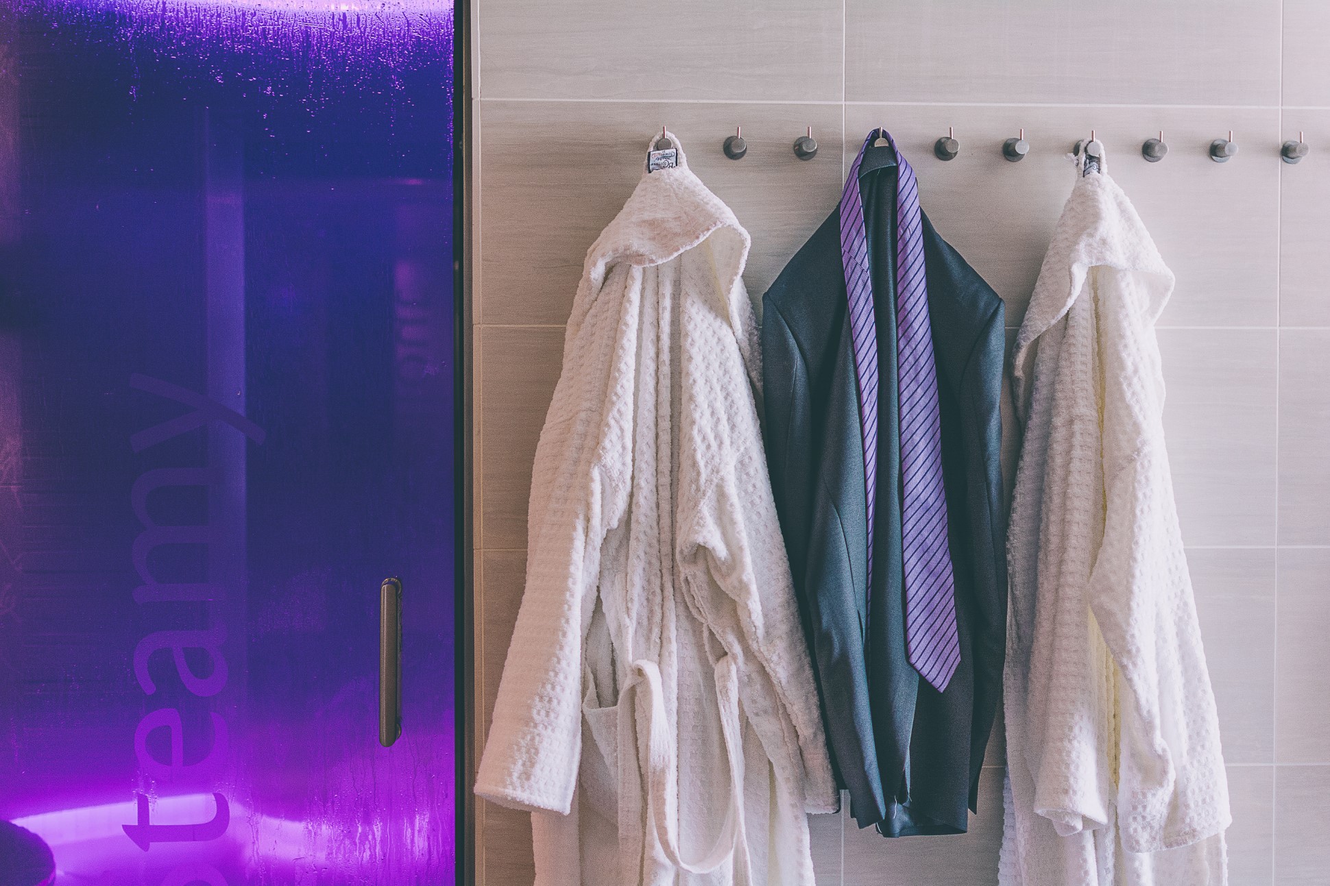 three robes and jacket with tie hanging on hooks