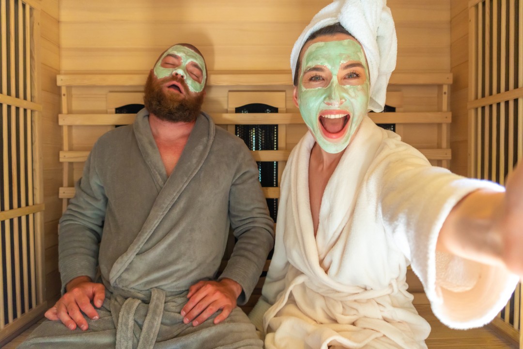 couple in robes with face masks in small wooden sauna