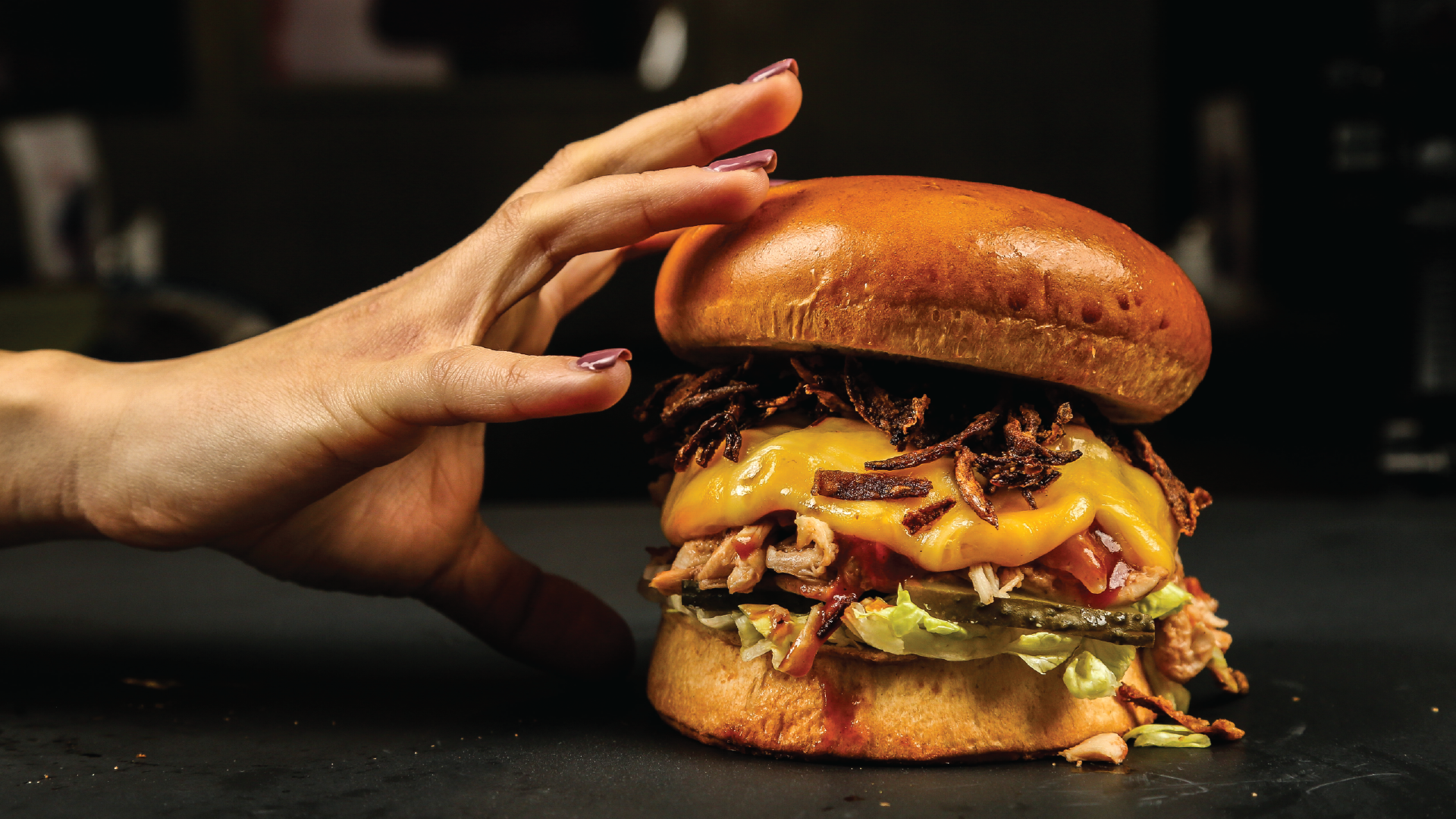 hand reaching for burger with cheese lettuce and sauce