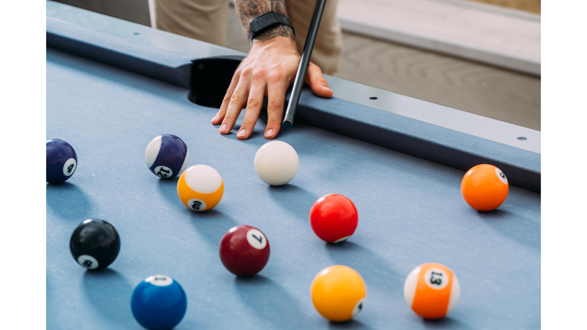 hand aiming cue ball on blue pool table with balls