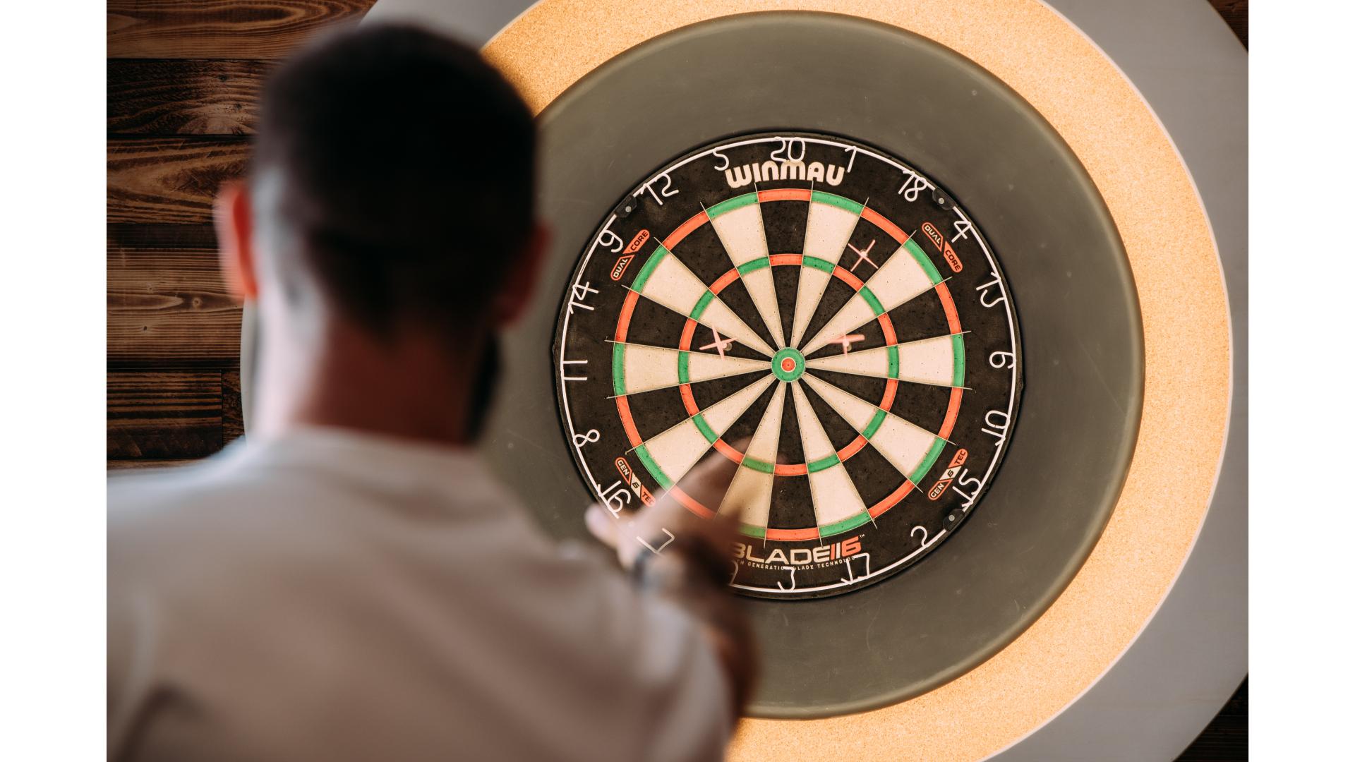 man playing darts throwing dart at dartboard