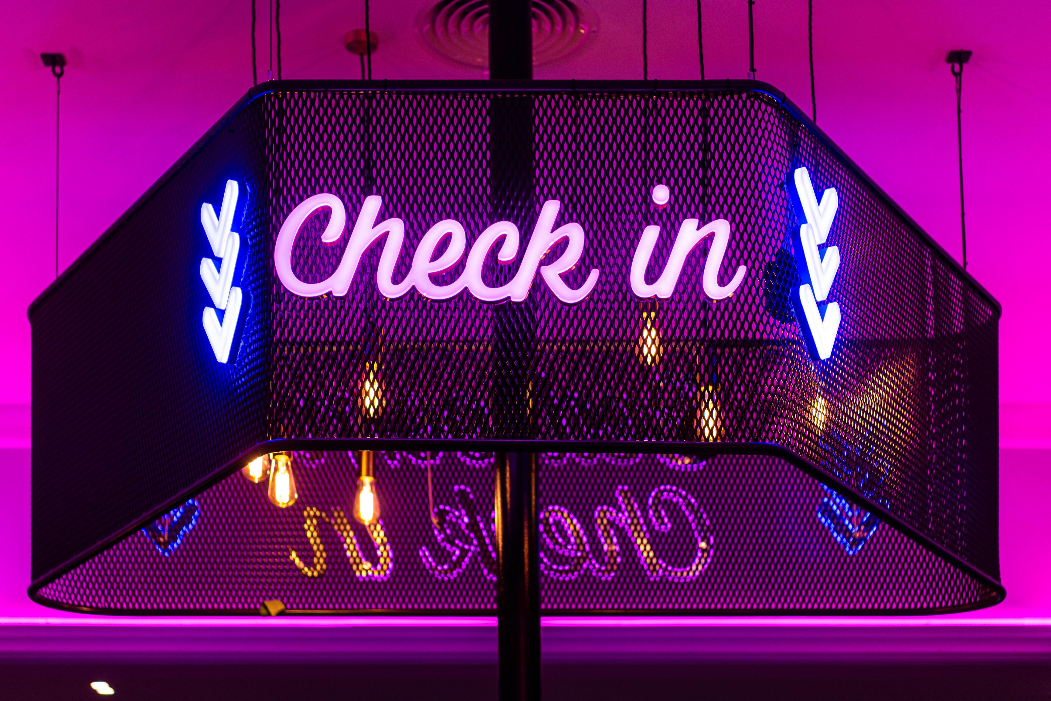 neon check in sign with blue arrows on pink background