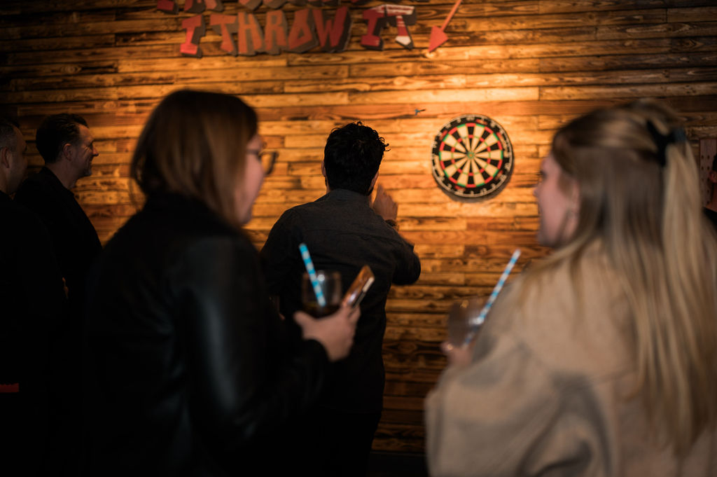 people playing darts in dimly lit bar with drinks