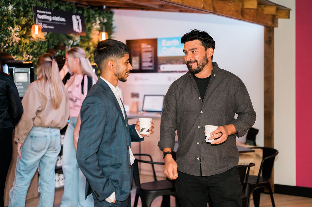 two men holding coffee cups chatting indoors