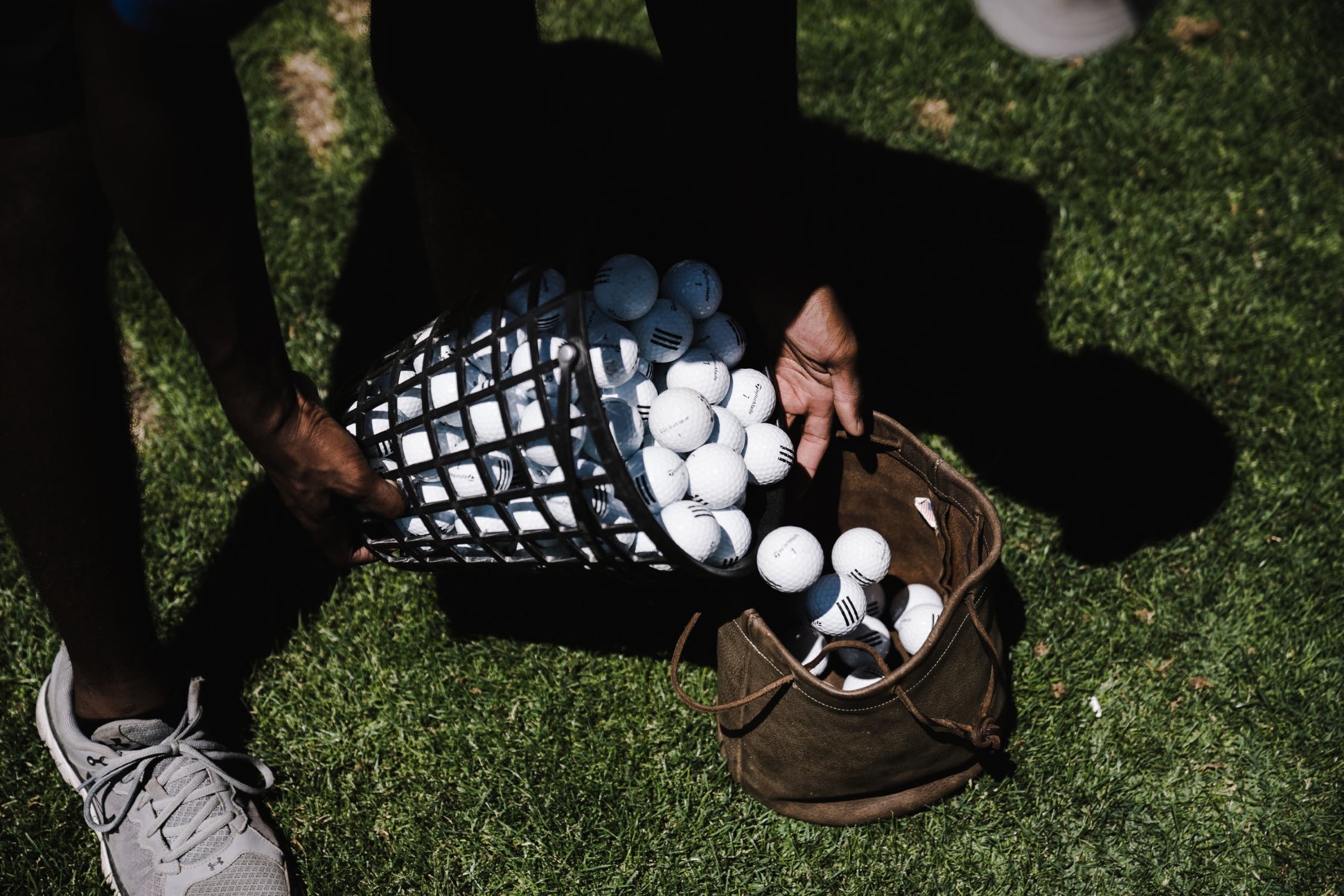person pouring white golf balls from basket to bag on